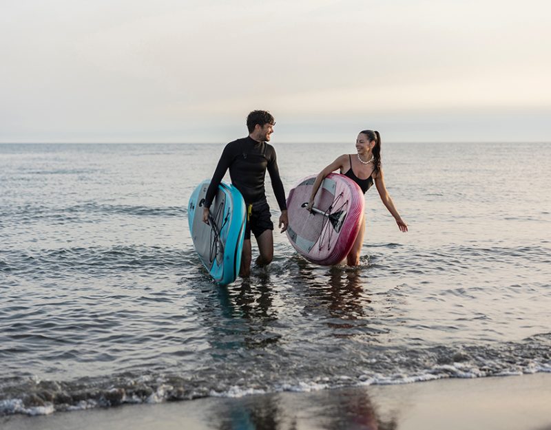Smiling couple walking out of the sea after an invigorating stand up paddling session, carrying their boards and savoring the beautiful sunset together