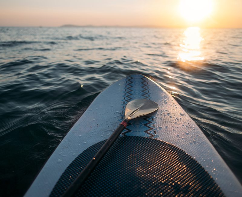 Paddleboard with paddle on sunset sea