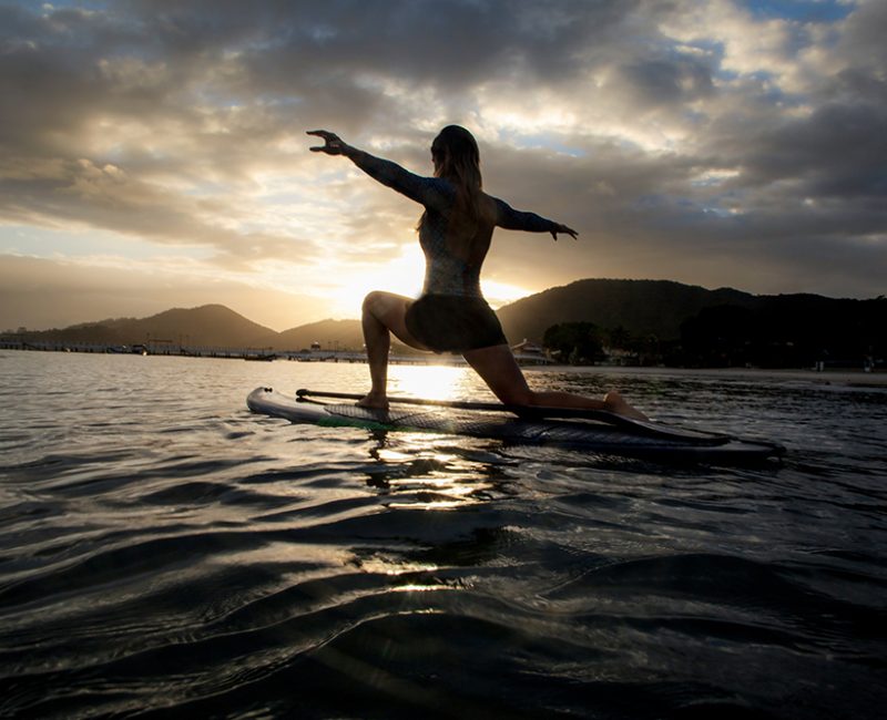 Woman with open arms over stand Up paddle at sunrise, Brazilian